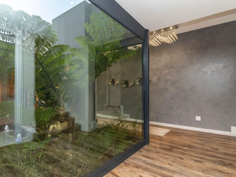 Modern living area featuring high-end timber flooring, a textured feature wall, and a striking glass-enclosed internal courtyard garden.