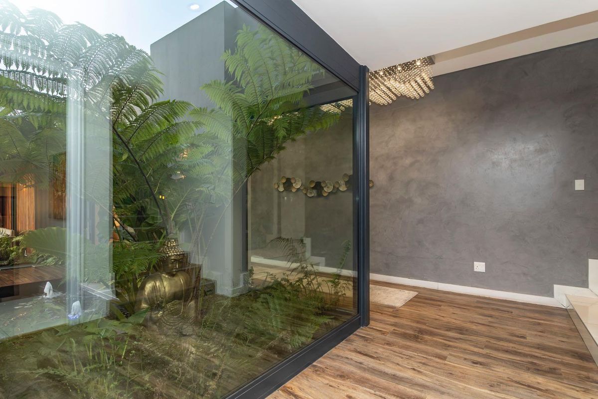 Modern living area featuring high-end timber flooring, a textured feature wall, and a striking glass-enclosed internal courtyard garden.