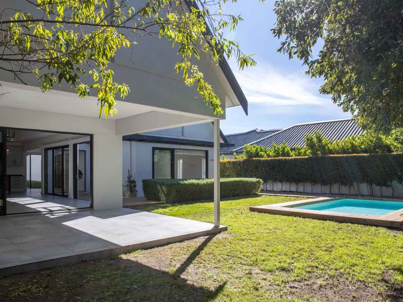 Rear view of the property featuring a covered patio, a well-maintained lawn, and a swimming pool with timber decking.