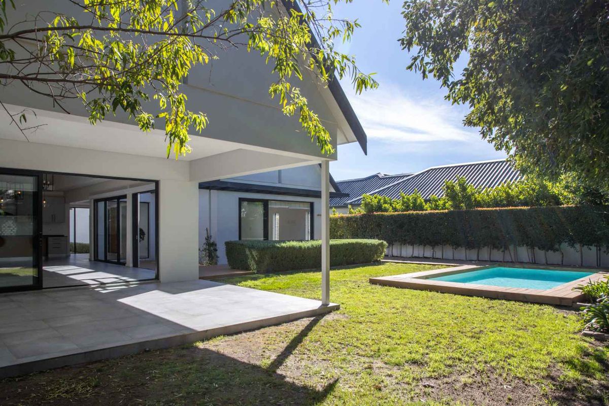 Rear view of the property featuring a covered patio, a well-maintained lawn, and a swimming pool with timber decking.
