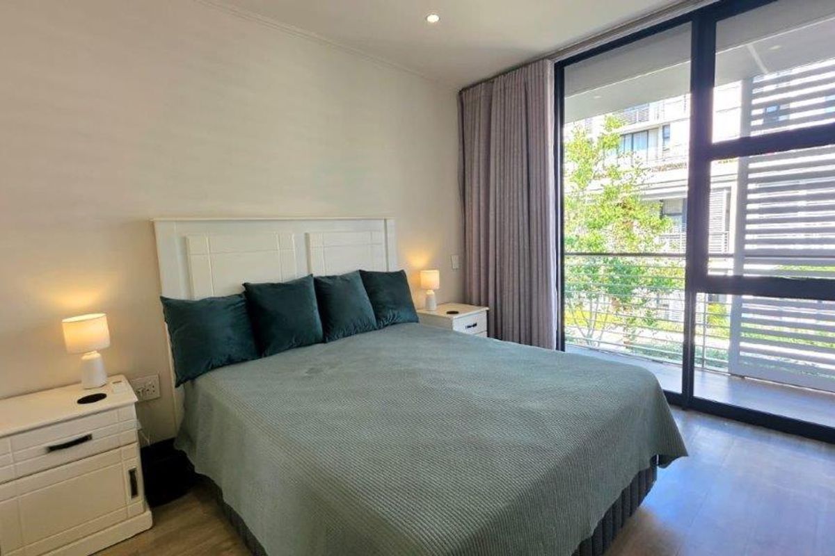 A well-maintained bedroom featuring laminate flooring, recessed lighting, and a large sliding glass door providing access to an outdoor balcony area.