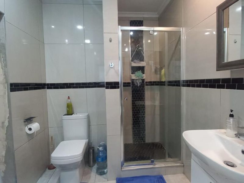 A functional bathroom featuring a glass-enclosed shower, modern toilet, and vanity basin with neutral wall tiling and a decorative black accent border.