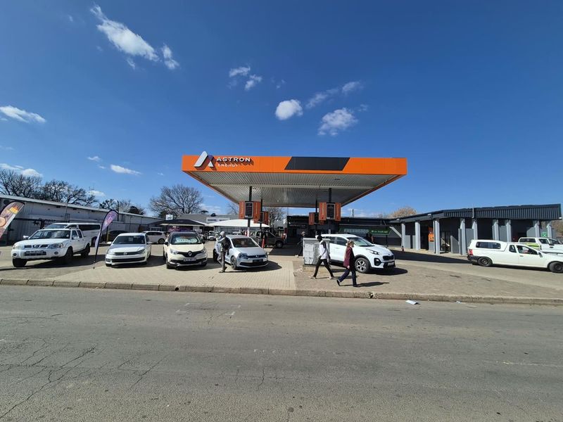 A commercial fuel station forecourt featuring an Astron Energy canopy, paved driveway, and adjacent retail building.