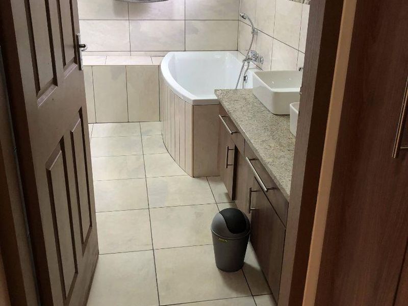 A functional bathroom featuring a built-in vanity with a stone countertop, vessel sink, and a tiled bathtub with integrated shower fixtures.
