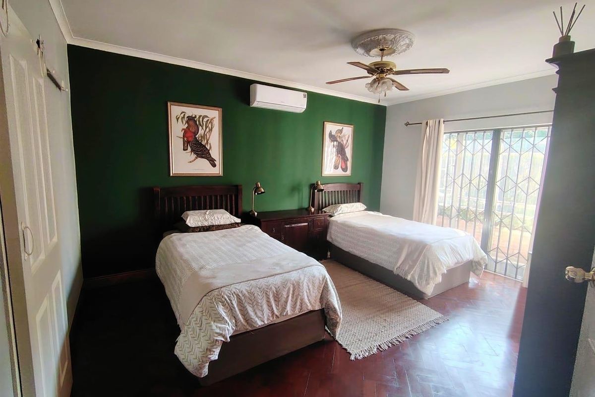 Spacious bedroom featuring dark parquet flooring, a ceiling fan with decorative rose, split-system air conditioning, and sliding glass doors with security gates.