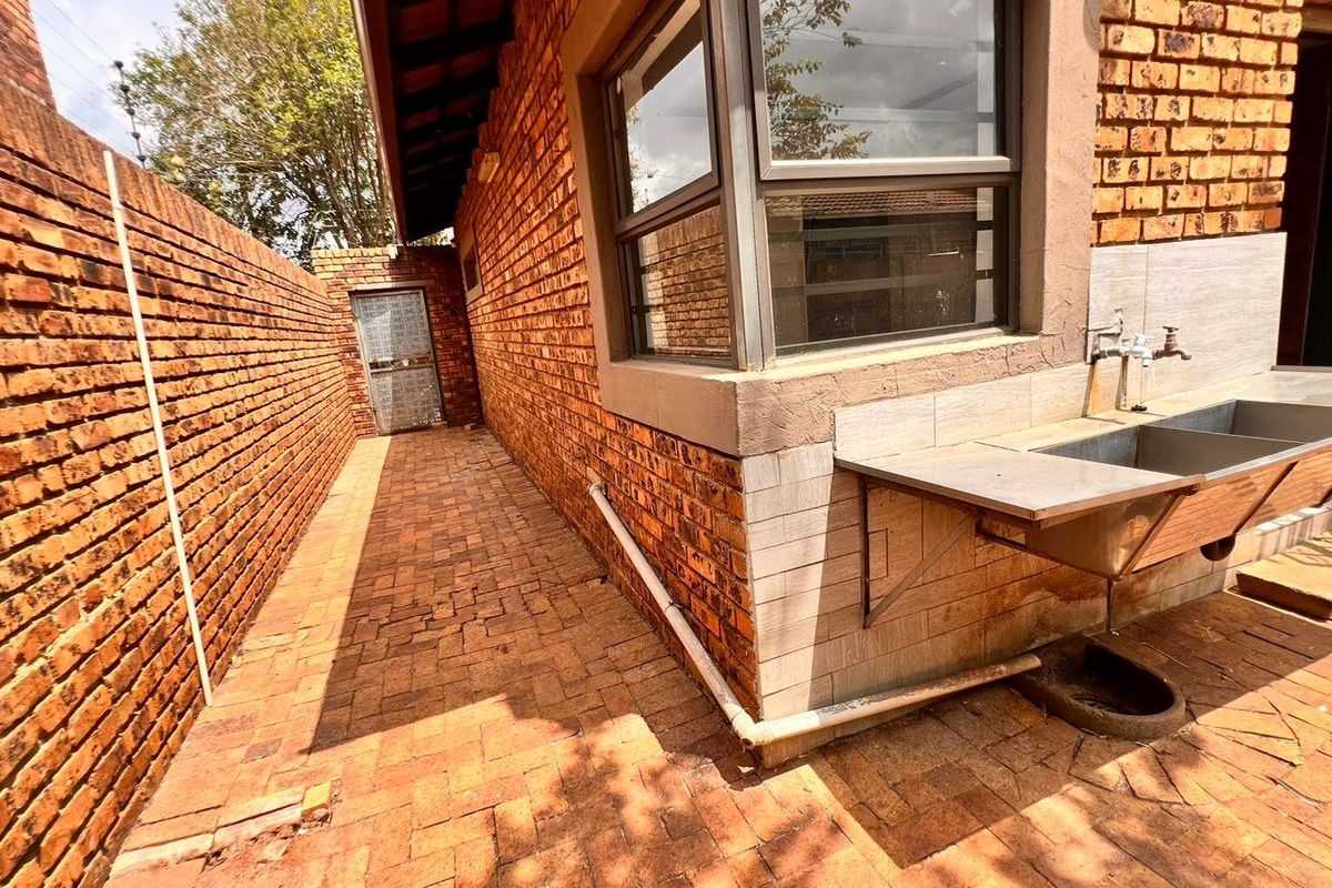 Exterior side passage featuring a brick-paved walkway, exposed brick walls, and a functional stainless steel utility sink with plumbing fixtures.