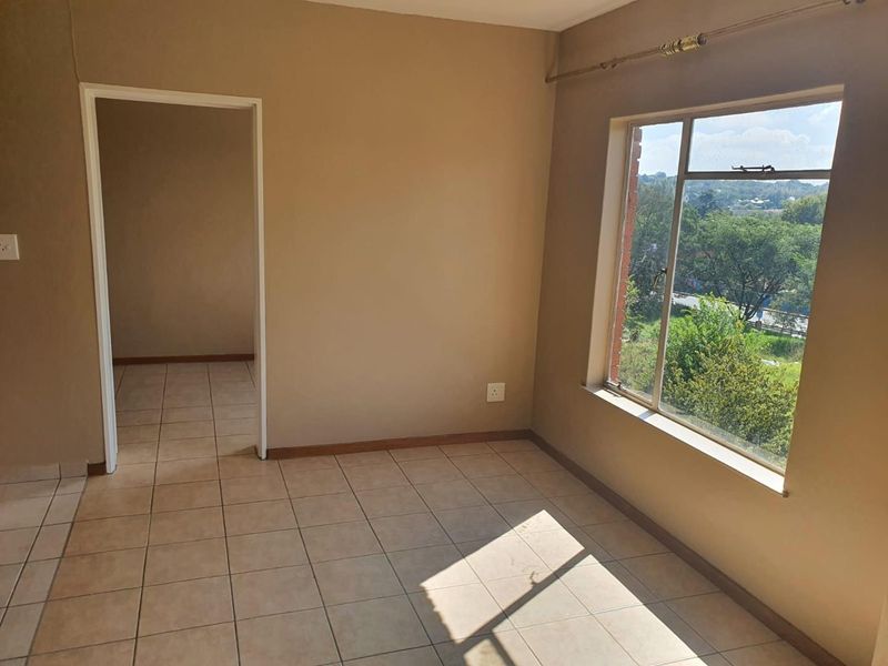 An empty bedroom featuring tiled flooring, a large window with natural light, and a neutral wall finish, ready for personalization.