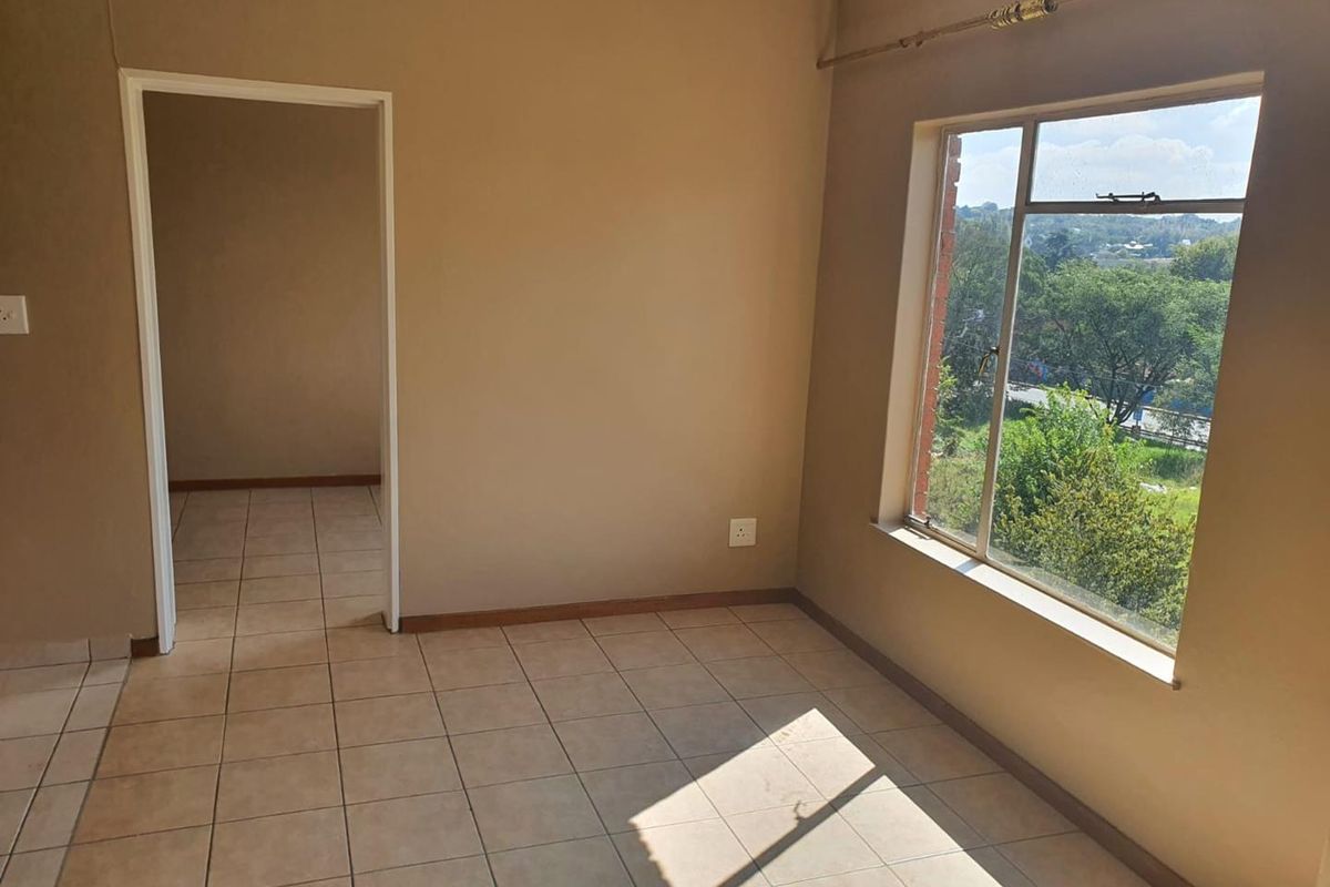 An empty bedroom featuring tiled flooring, a large window with natural light, and a neutral wall finish, ready for personalization.