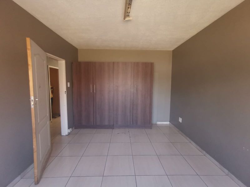 An empty bedroom featuring tiled flooring and built-in wooden cupboards, providing a neutral canvas for personalization.