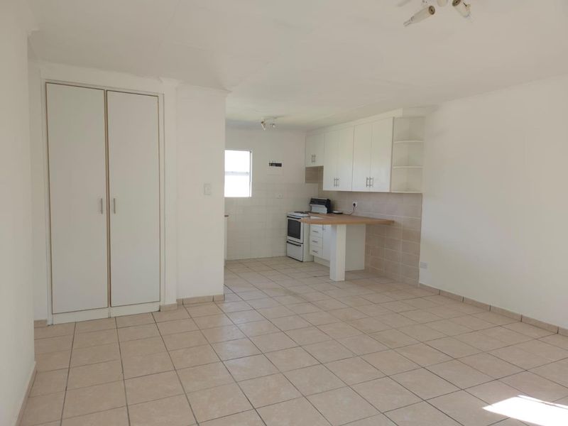 An open-plan living and kitchen area featuring tiled flooring, built-in cupboards, and a functional kitchen layout with a breakfast counter.