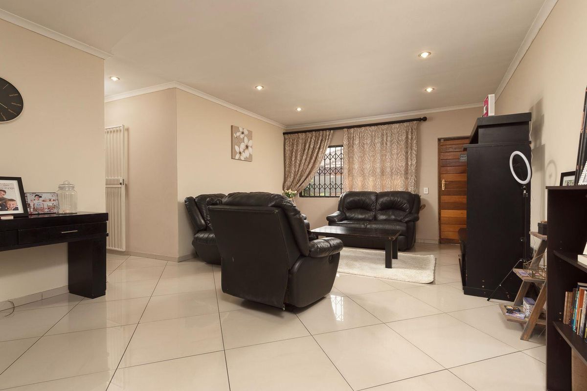 A spacious living room featuring large format floor tiles, recessed downlighting, and a secure window with burglar bars.