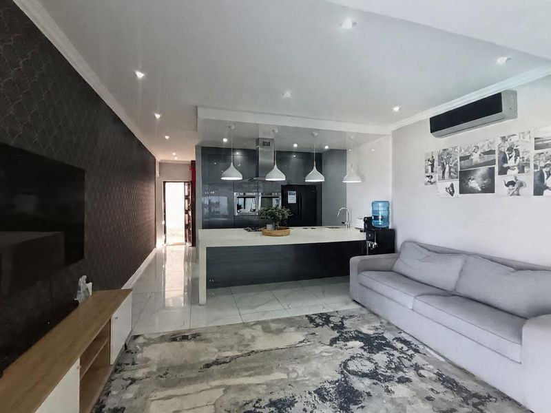 Modern open-plan living area featuring a sleek kitchen with a central island, built-in appliances, recessed lighting, and polished tiled flooring.