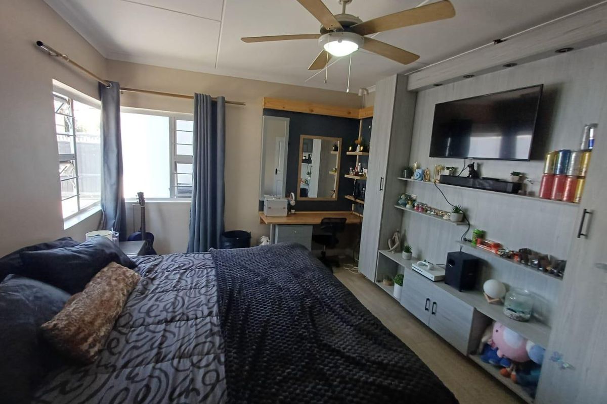 A well-lit bedroom featuring a built-in wall unit with integrated shelving, a ceiling fan, and a dedicated built-in desk area.