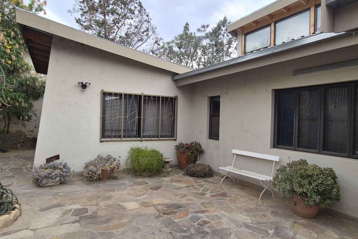 A rear patio area featuring stone paving, security-fitted windows, and a unique architectural roofline with clerestory windows.