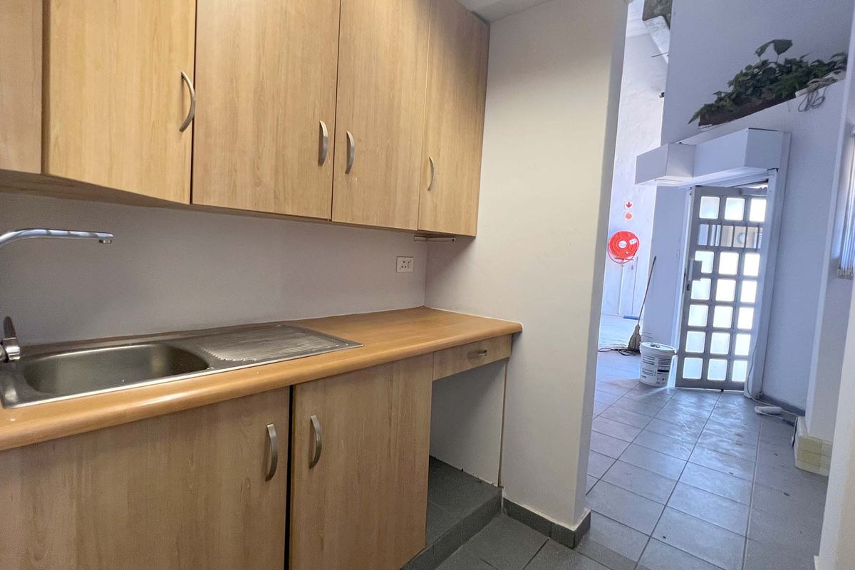 A functional kitchenette area featuring wood-look cabinetry, a stainless steel sink, and tiled flooring, providing convenient utility space within the industrial unit.