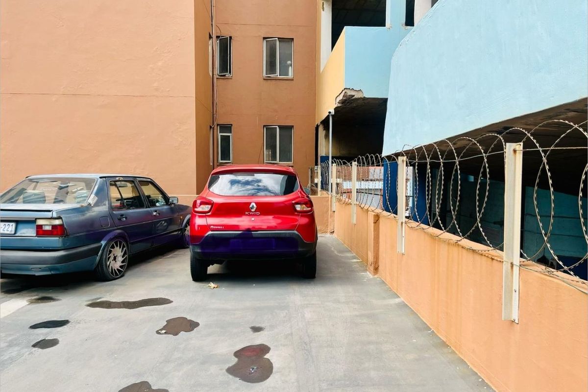 Rear exterior area of the apartment building featuring concrete paving, perimeter wall with razor wire, and visible structural wear on the building facade.