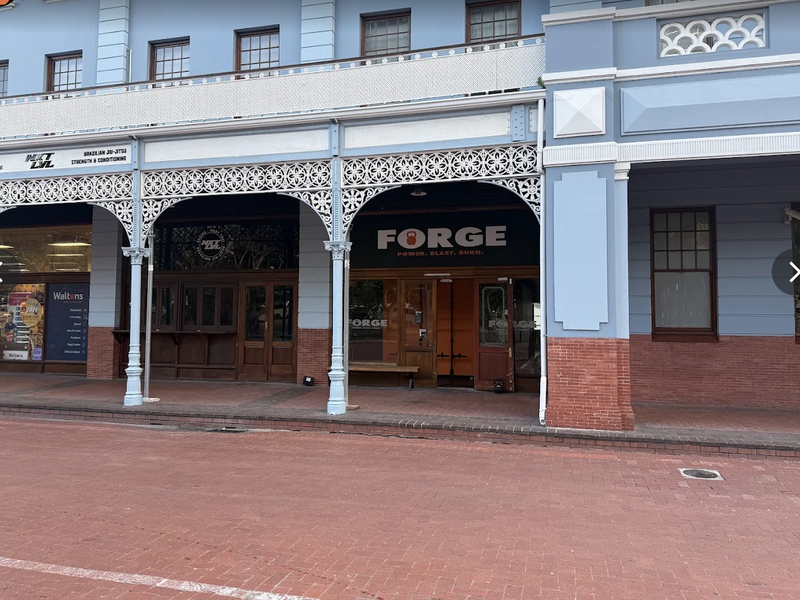 A well-maintained commercial storefront featuring ornate ironwork detailing, brick accents, and large timber-framed windows along a paved street-level entrance.