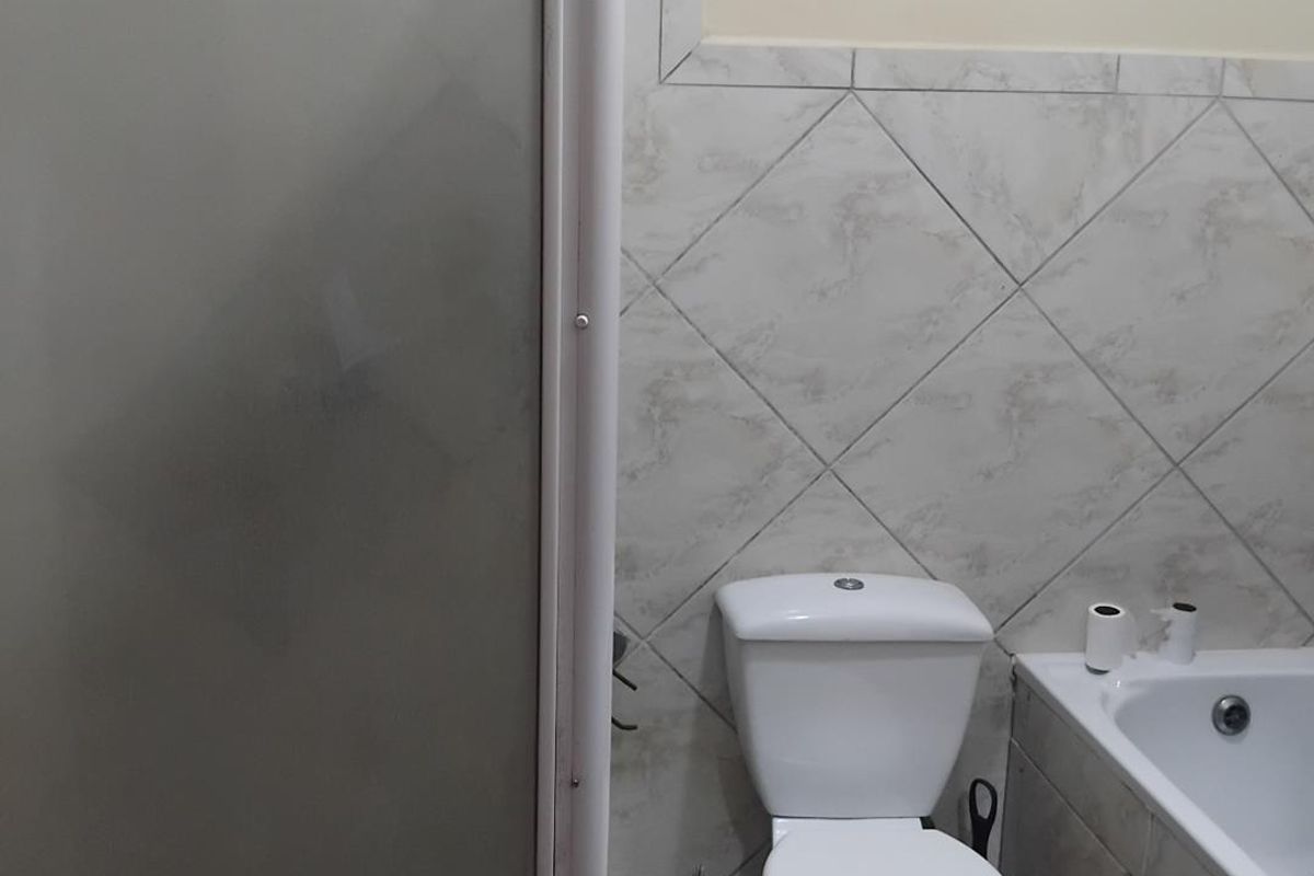 A functional bathroom featuring a standard toilet, a bathtub with tiled surround, and a shower enclosure with a frosted glass screen.