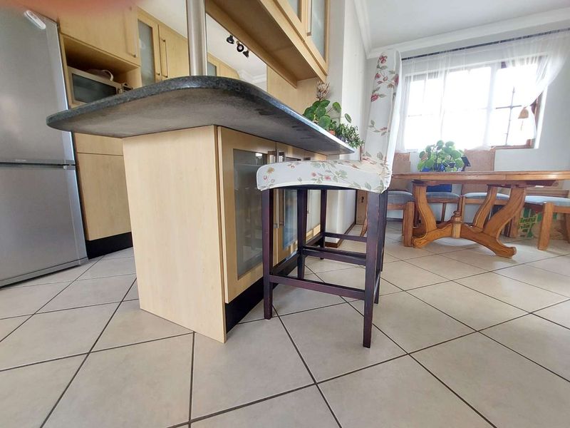 A kitchen area featuring light wood cabinetry, a breakfast bar with a stone countertop, and tiled flooring throughout.