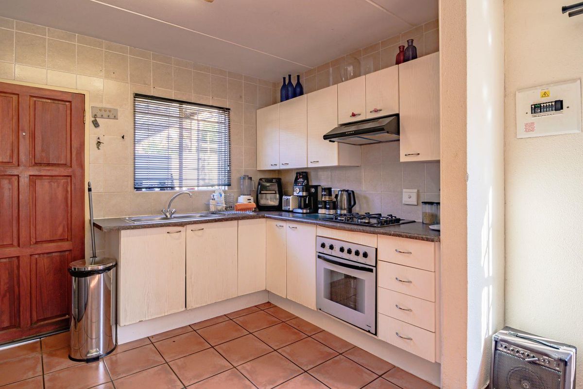 A functional kitchen featuring light-toned cabinetry, a built-in oven with gas hob, extractor fan, and tiled flooring with direct access to an exterior door.