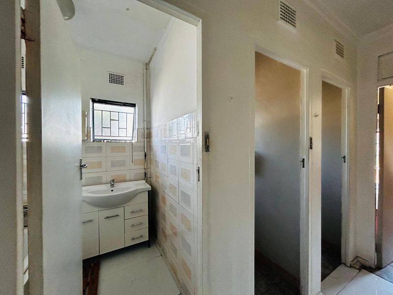 A functional bathroom area featuring a vanity basin, tiled walls, and multiple doorways leading to separate utility or toilet compartments.