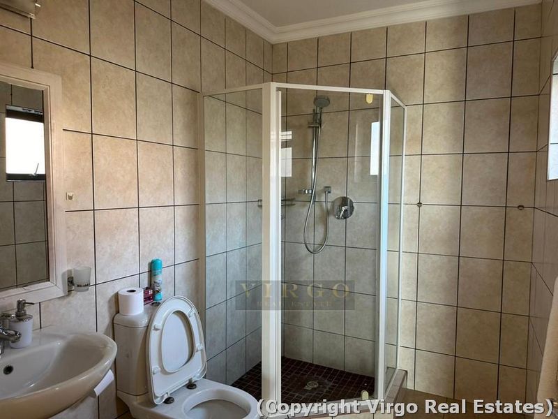 A functional bathroom featuring a corner shower enclosure, pedestal basin, and toilet with neutral wall tiling throughout.