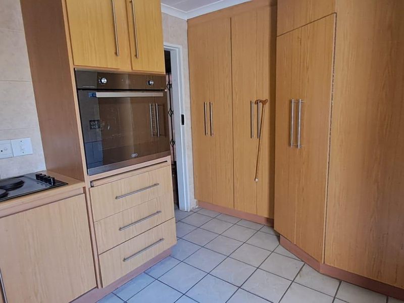 A functional kitchen featuring light wood-look cabinetry, built-in oven, electric hob, and tiled flooring, offering a practical layout with ample storage space.