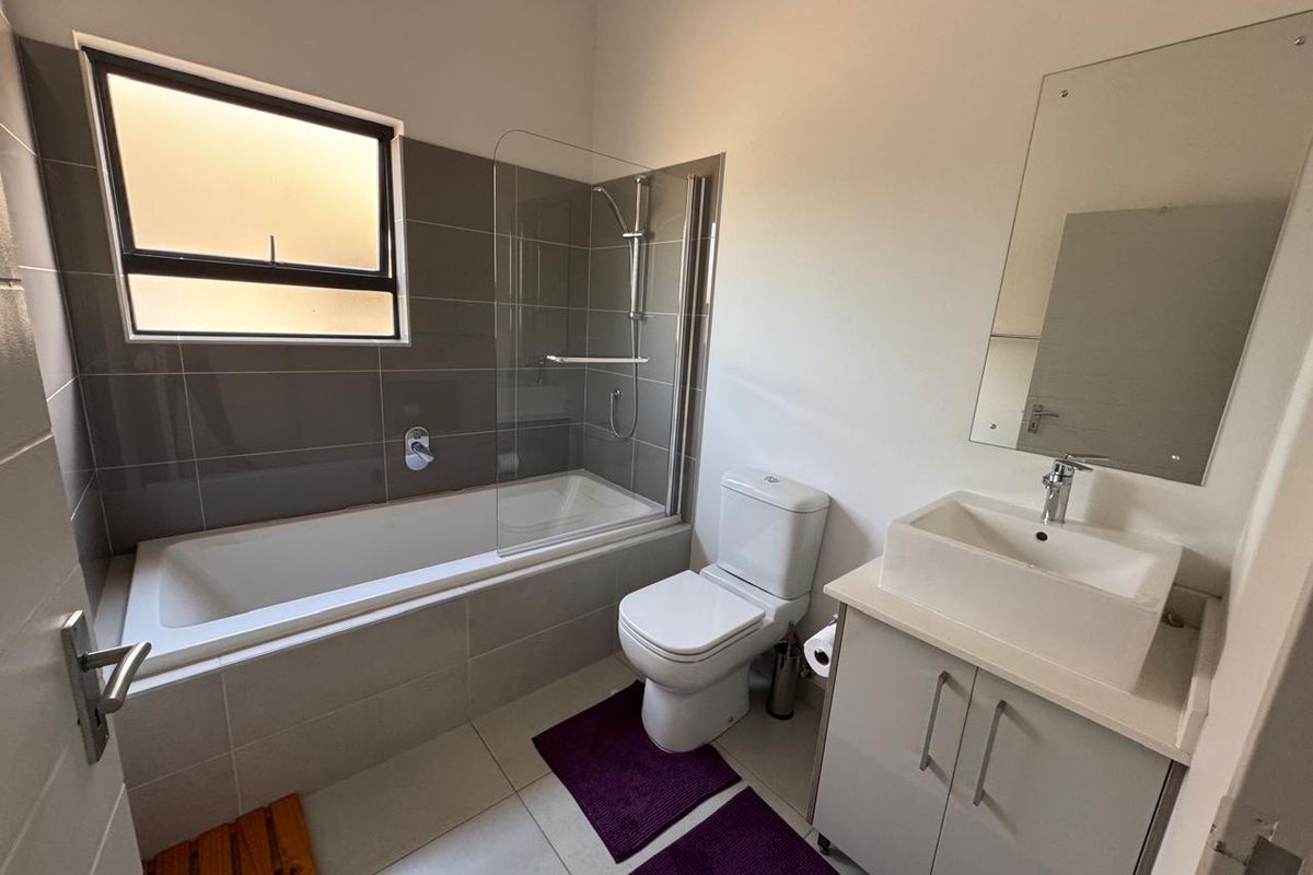 A clean, modern bathroom featuring a bathtub with a glass shower screen, a vanity with a basin, and a toilet.