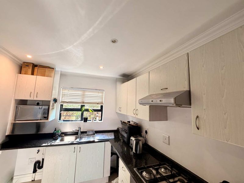 A functional kitchen featuring light wood-grain cabinetry, dark granite countertops, a gas hob with extractor fan, and a stainless steel sink.