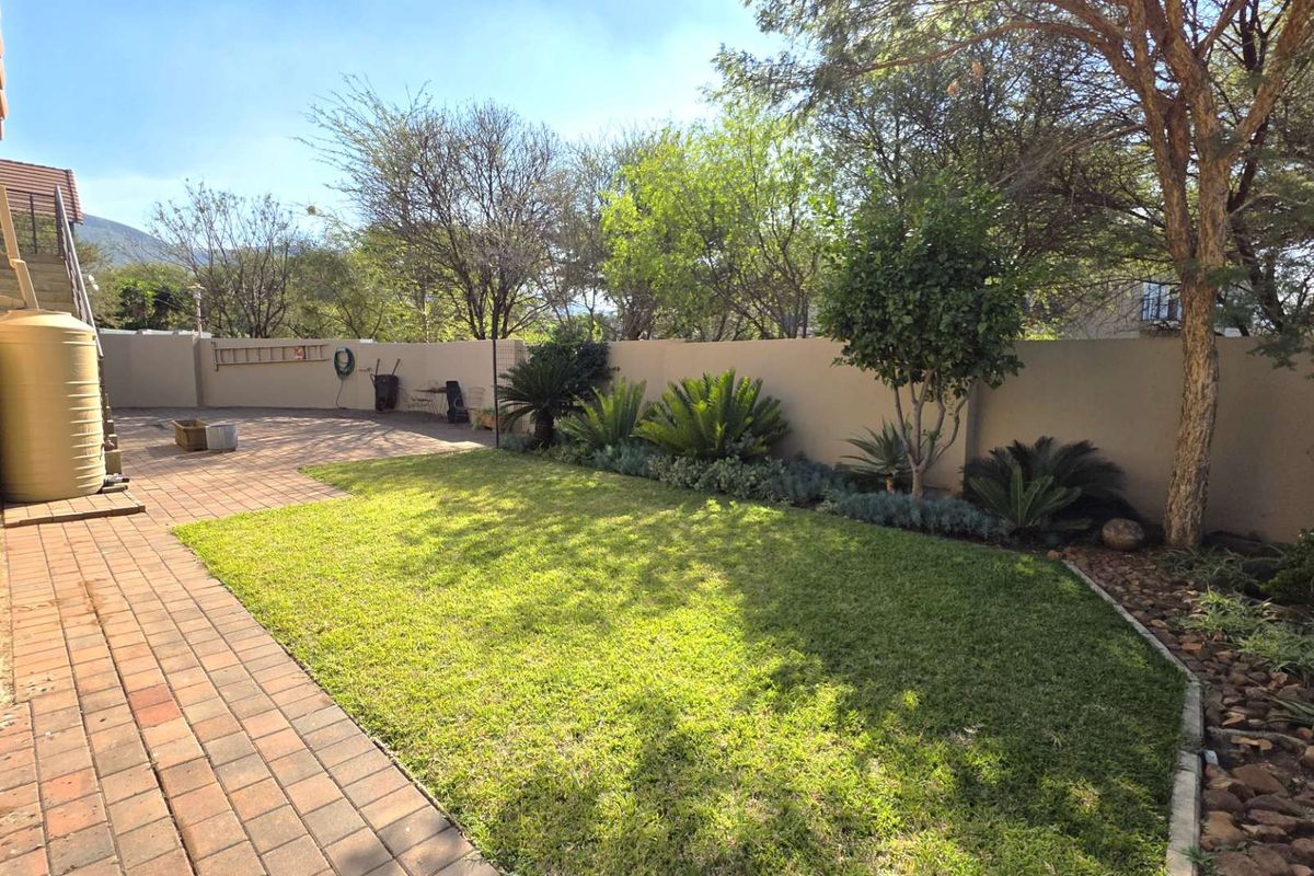 A well-maintained rear garden featuring a paved patio area, a manicured lawn, and established perimeter landscaping with a boundary wall.