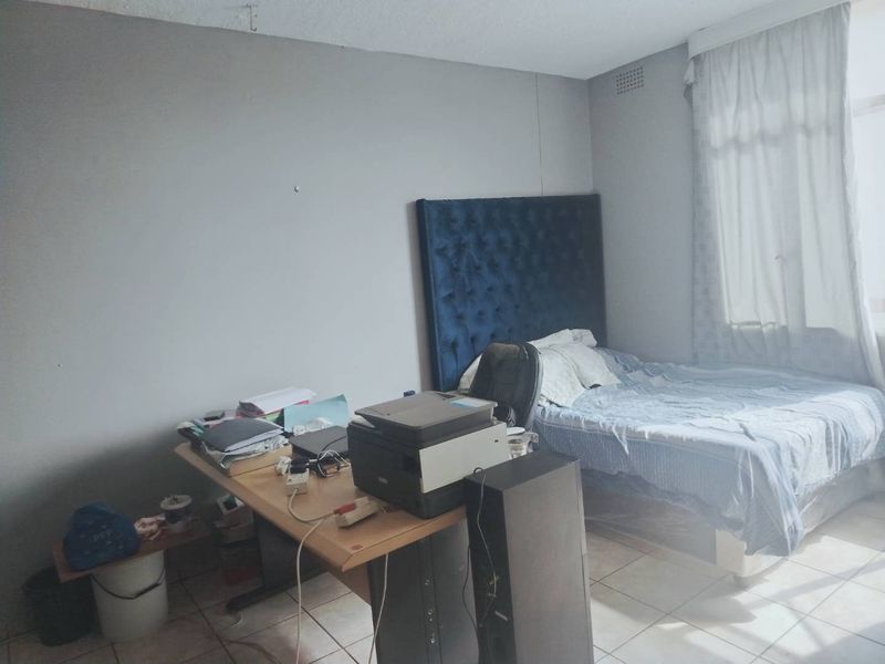 A bedroom featuring tiled flooring and a window with a curtain rail, requiring cosmetic updates to improve its overall condition.