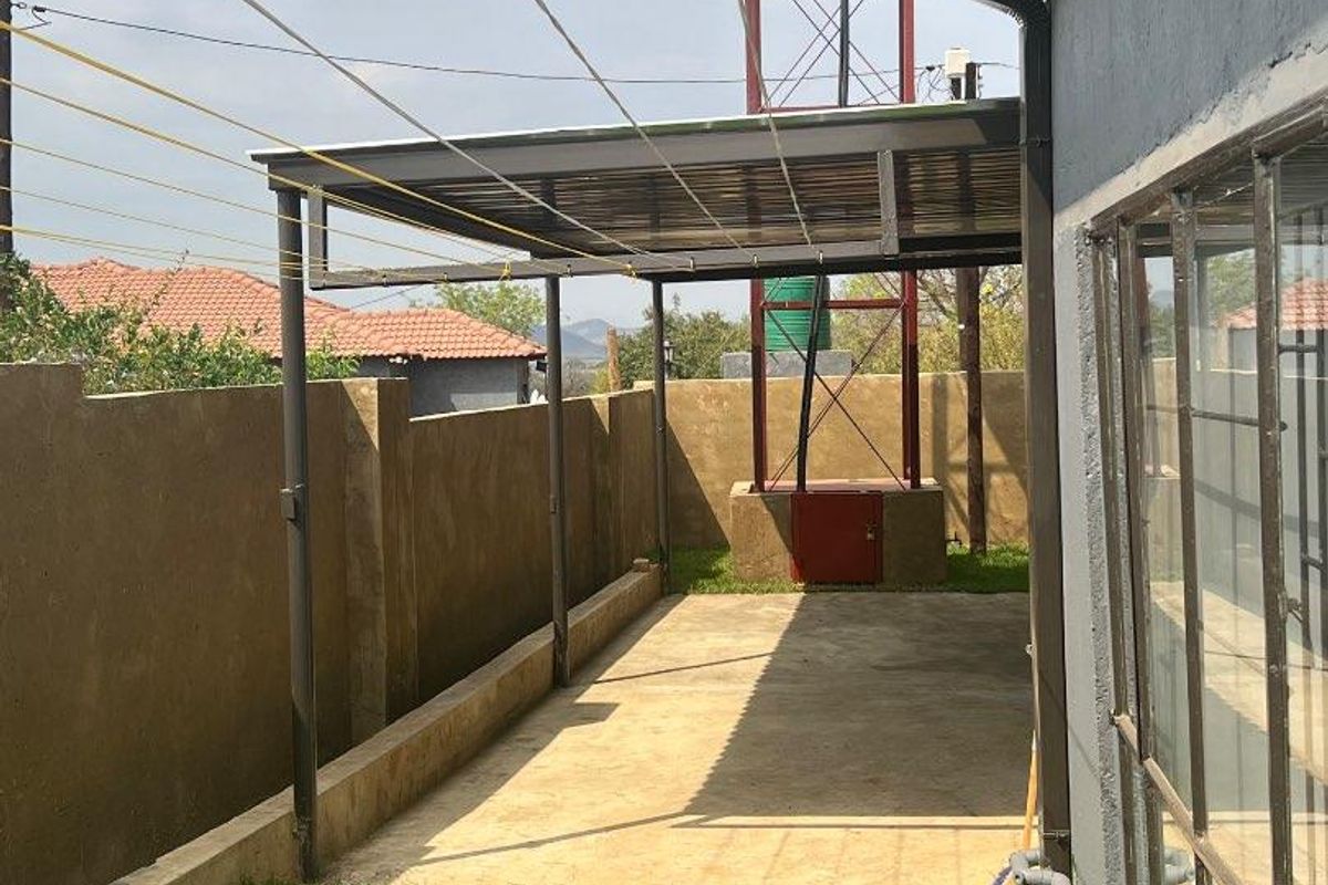 A rear exterior area featuring a covered patio, concrete flooring, a water tank on a steel stand, and a small lawn with paved stepping stones.