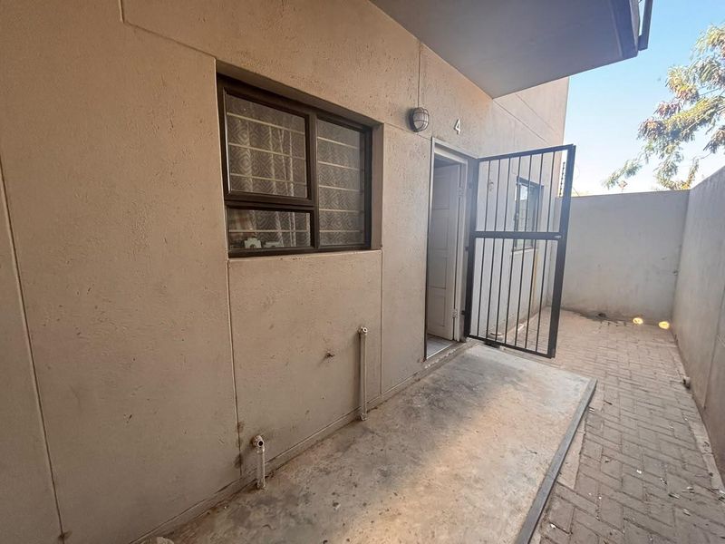 A private rear courtyard area featuring paved flooring, a security gate, and external plumbing connections for utility use.