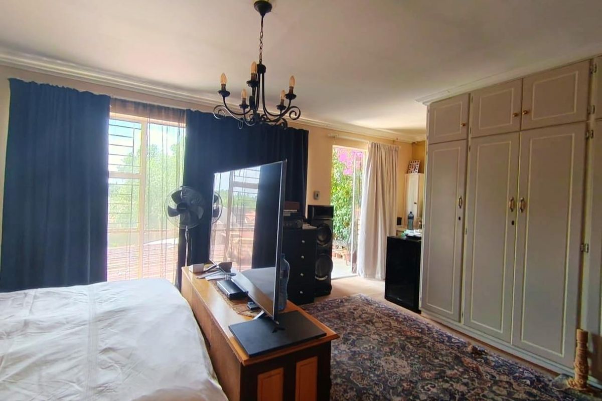 Spacious bedroom featuring built-in cupboards, large windows with security bars, and direct access to an outdoor patio area.
