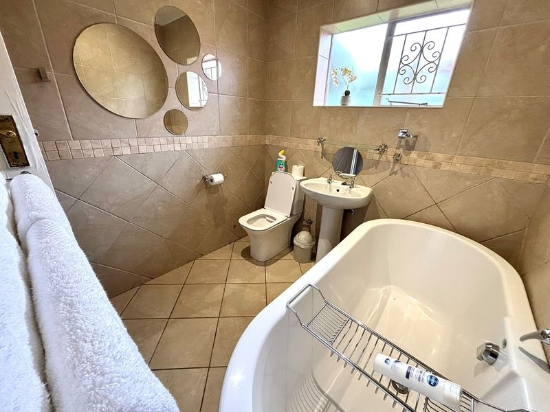 A functional bathroom featuring a pedestal basin, toilet, and a freestanding bathtub with neutral wall and floor tiling.