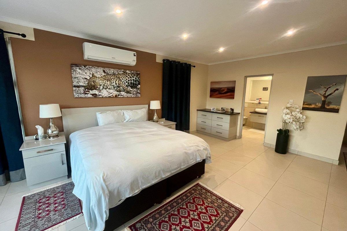Spacious bedroom featuring tiled flooring, recessed downlighting, a wall-mounted air conditioning unit, and direct access to an en-suite bathroom.