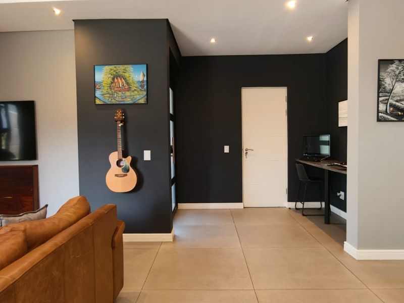 Modern open-plan living area featuring tiled floors, recessed lighting, a built-in workspace, and a sleek kitchen with dark subway tile backsplash.