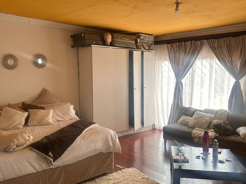 Spacious bedroom featuring laminate flooring, a built-in wardrobe, and large windows with security bars. The ceiling requires maintenance and cosmetic repair.