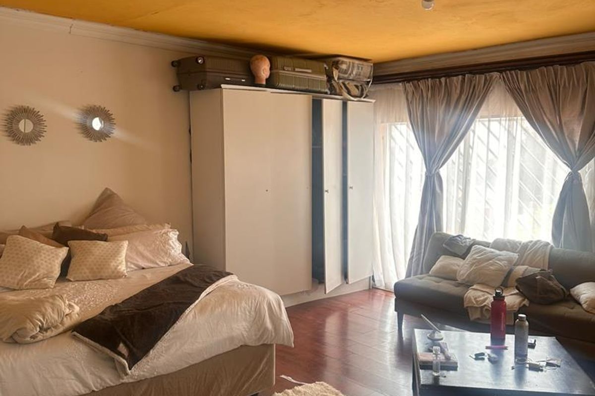 Spacious bedroom featuring laminate flooring, a built-in wardrobe, and large windows with security bars. The ceiling requires maintenance and cosmetic repair.