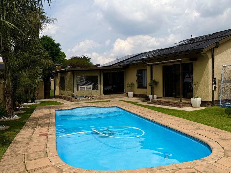 A well-maintained backyard featuring a swimming pool, paved surround, and a covered patio area with solar panels installed on the roof.