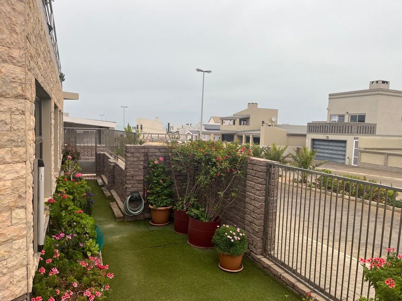 A well-maintained outdoor patio area featuring stone wall cladding, metal safety railings, and artificial turf flooring, overlooking the surrounding residential neighborhood.