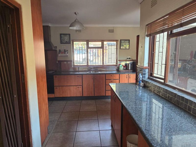 A functional kitchen featuring granite countertops, wooden cabinetry, and tiled flooring, with large windows providing natural light and security bars.