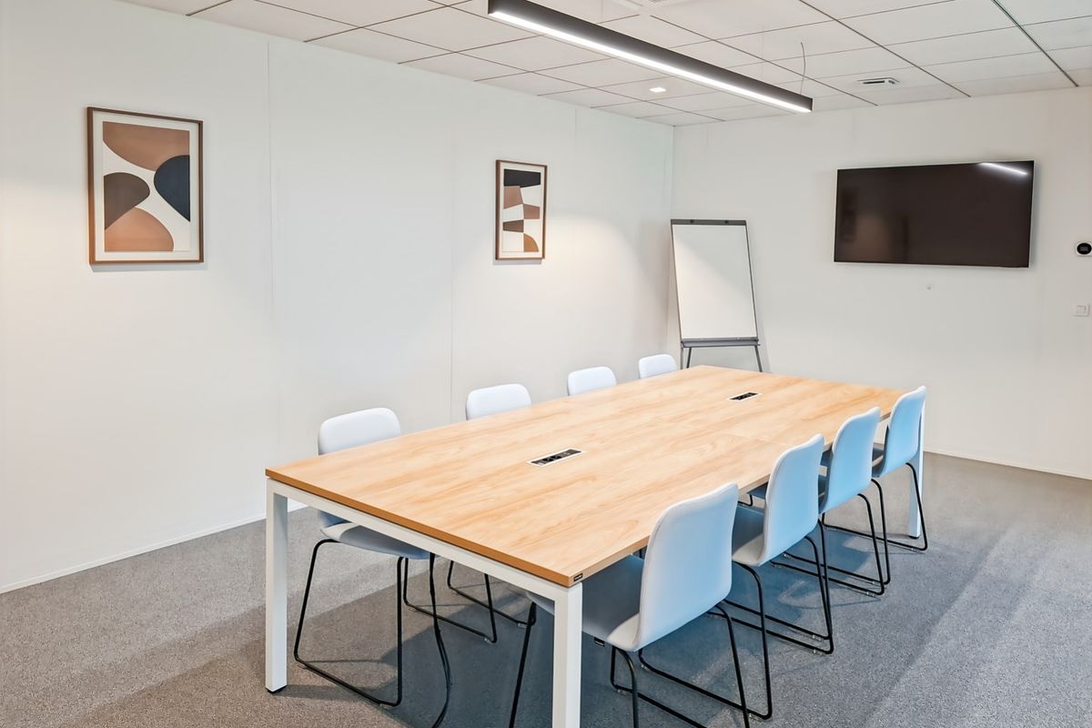 A modern, well-lit office meeting room featuring a large conference table, suspended lighting, and professional carpeted flooring.