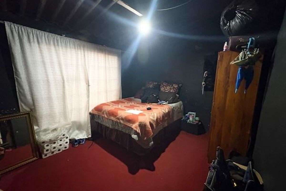 A bedroom featuring dark-painted walls, exposed ceiling rafters, and red carpeting, providing a basic sleeping space.