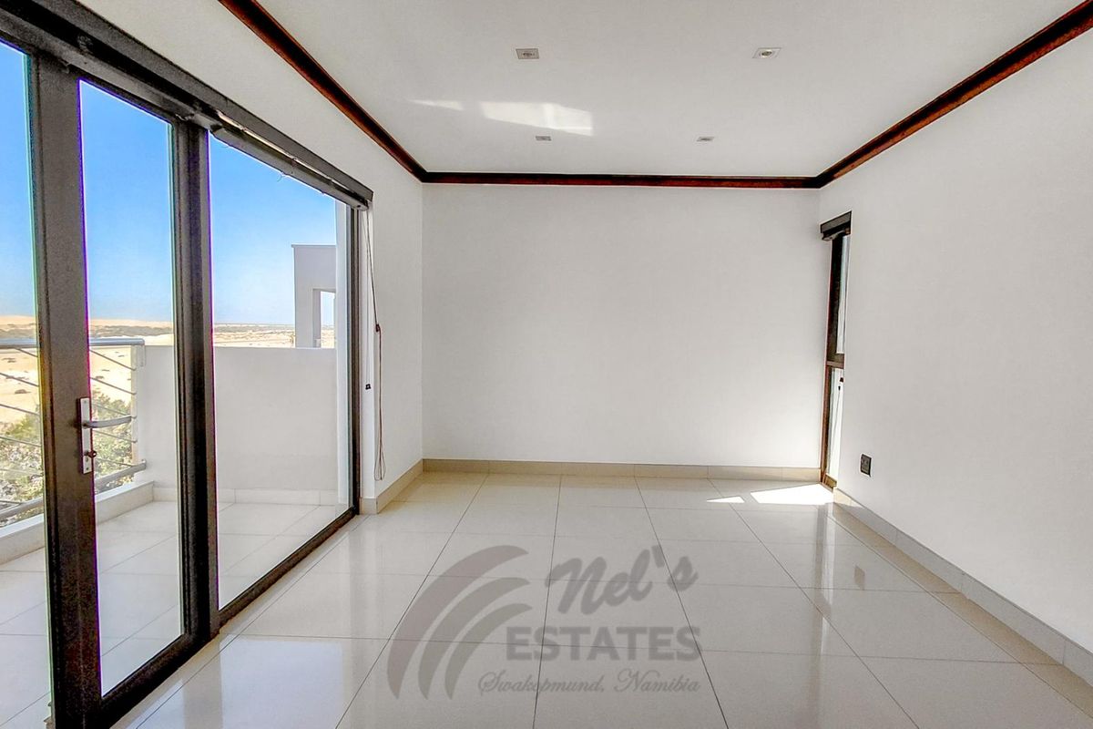 A bright, empty living room featuring large sliding glass doors that open onto a balcony with scenic desert views.