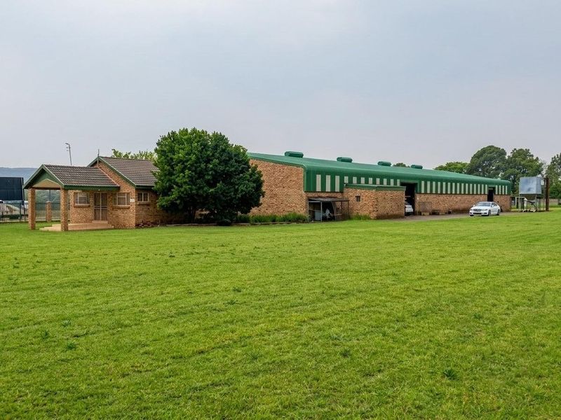 A commercial property featuring a large warehouse with a green metal roof and an attached face brick office building set on a spacious lawn.