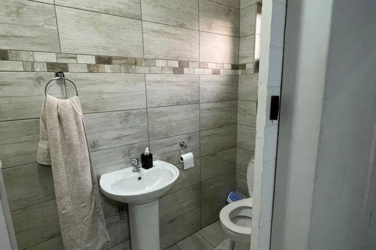 A compact bathroom featuring modern wood-look wall tiles, a white pedestal basin, and a standard toilet.
