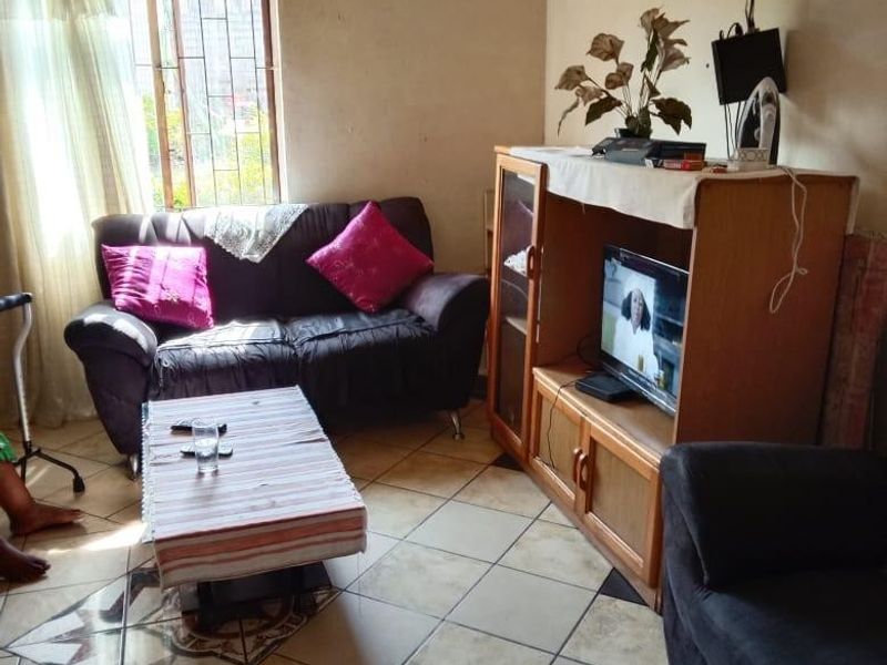 A living room featuring ceramic floor tiles and a window with security bars, requiring cosmetic updates to the wall finishes.