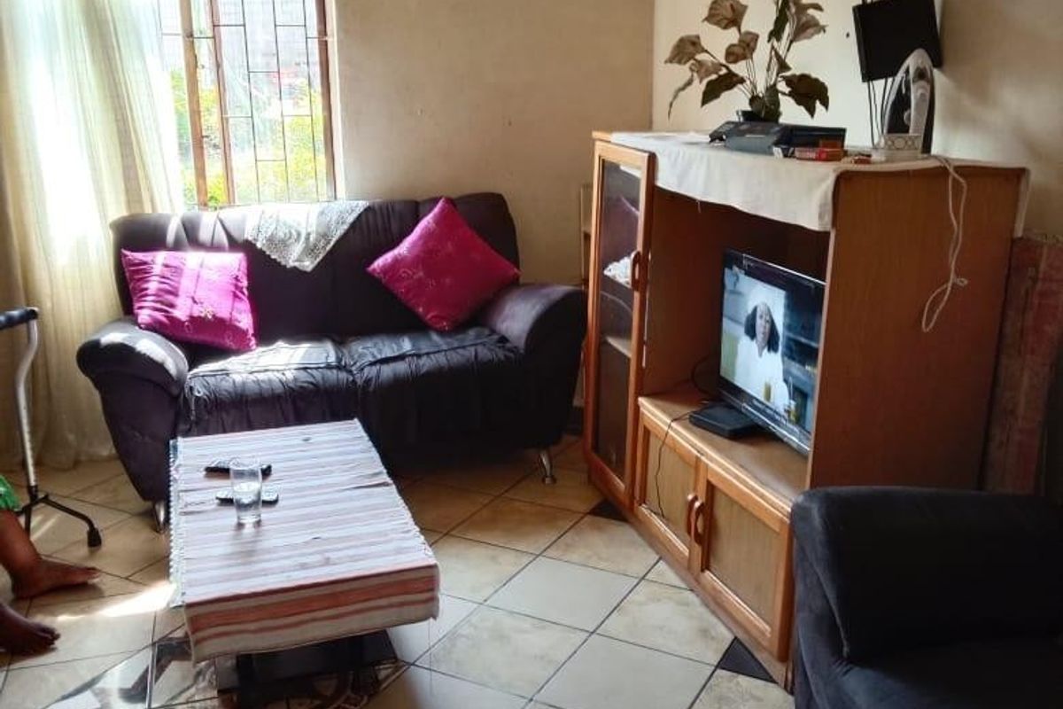 A living room featuring ceramic floor tiles and a window with security bars, requiring cosmetic updates to the wall finishes.