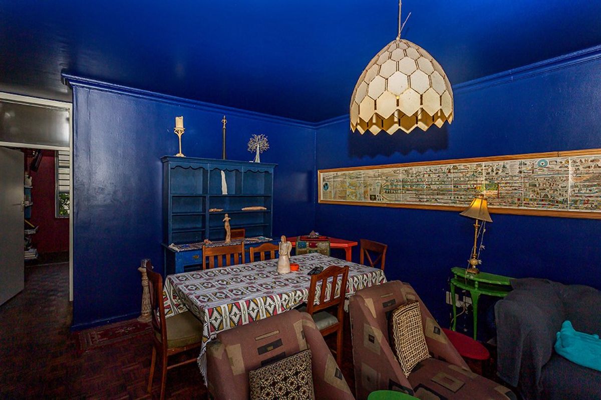 A living room featuring dark blue walls, parquet flooring, and a built-in shelving unit, offering a distinct and bold interior aesthetic.